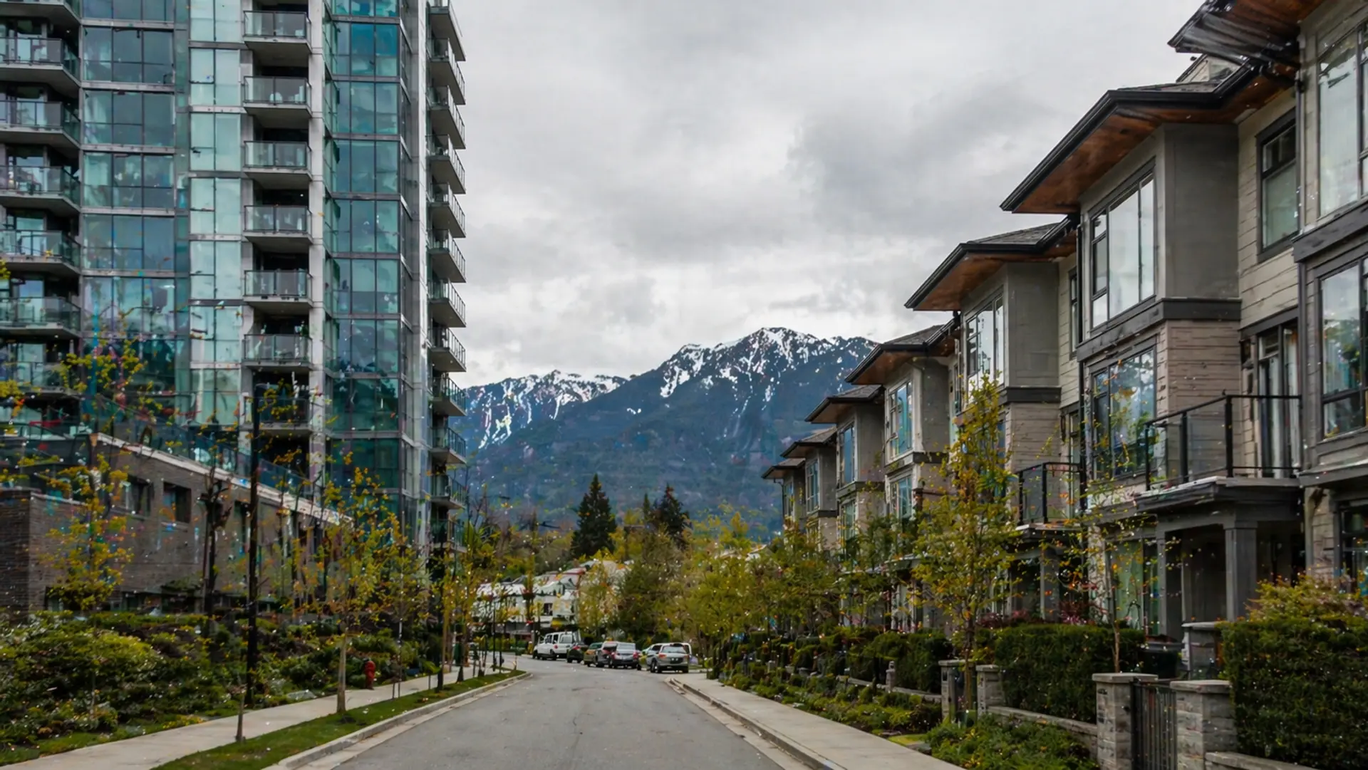 Glass condo tower beside a row of modern BC townhouses with North Shore mountains in background